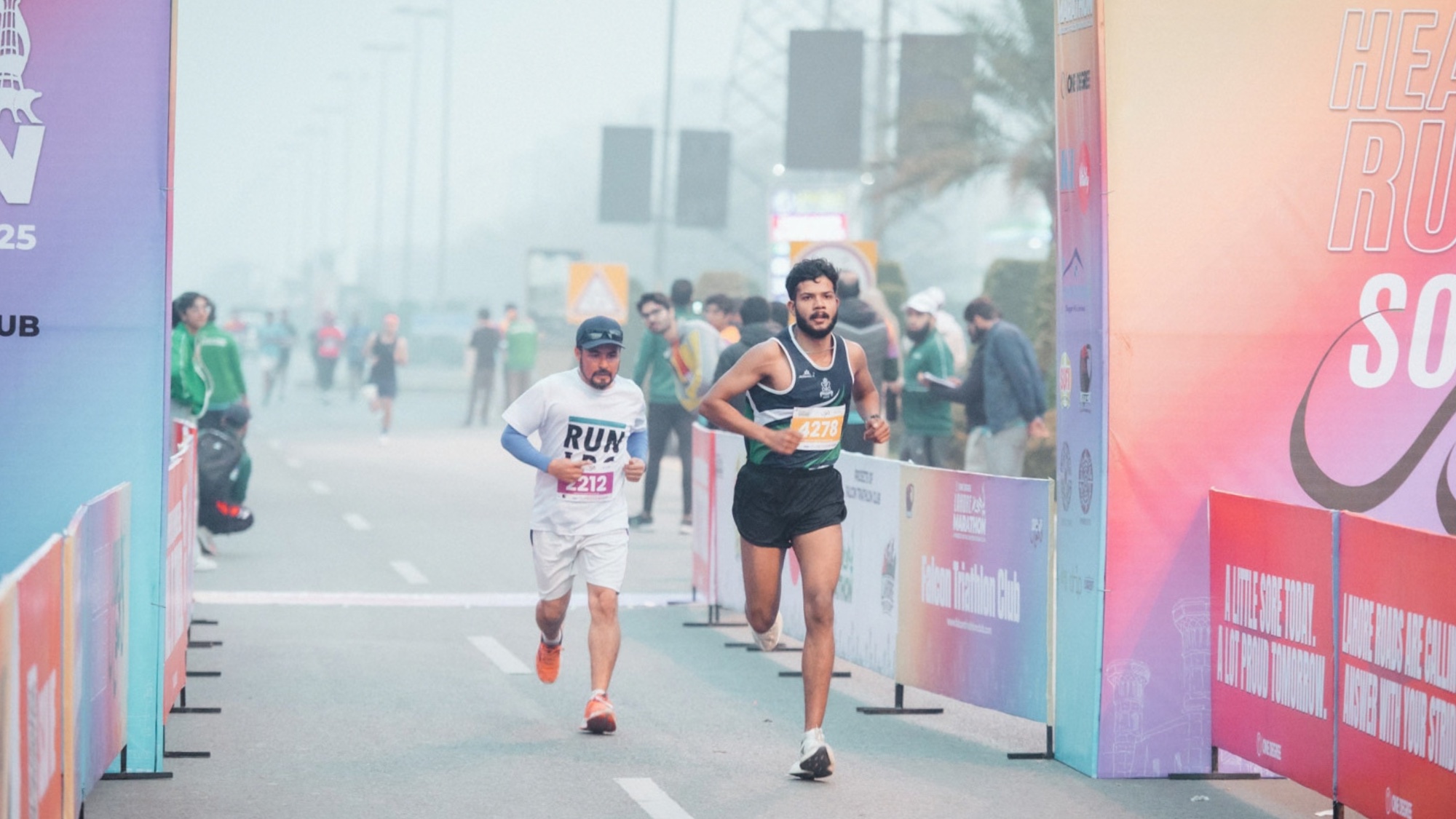 Two Lahore Marathon runners approaching the finish through early-morning mist