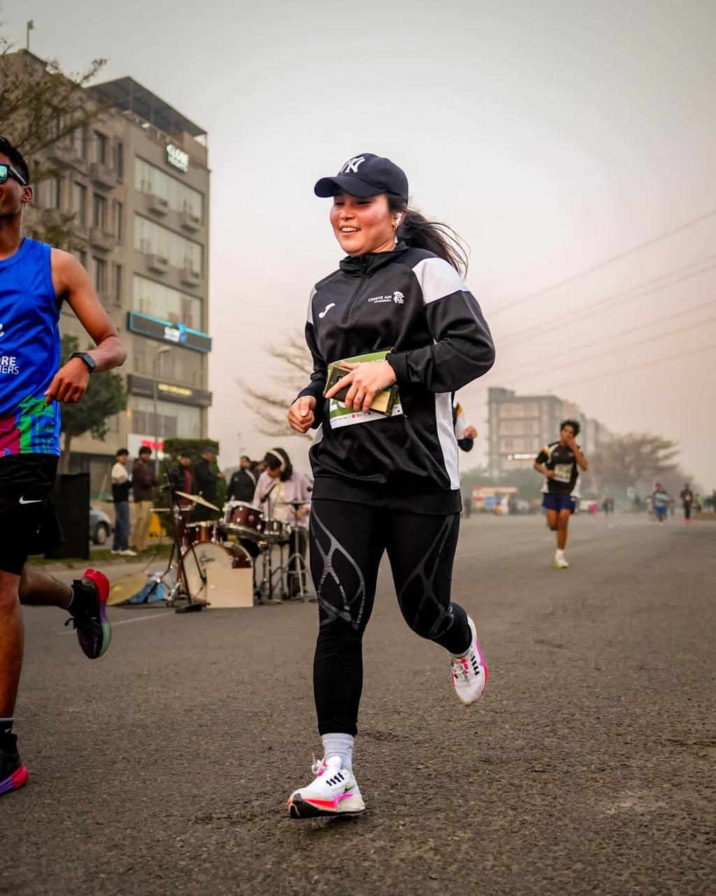 A woman in a cap running past a street drummer